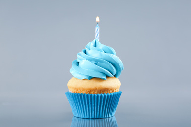 Photo of Delicious birthday cupcake with burning candle on light grey background