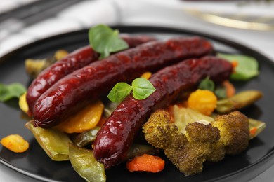 Photo of Delicious smoked sausages and baked vegetables on black plate, closeup