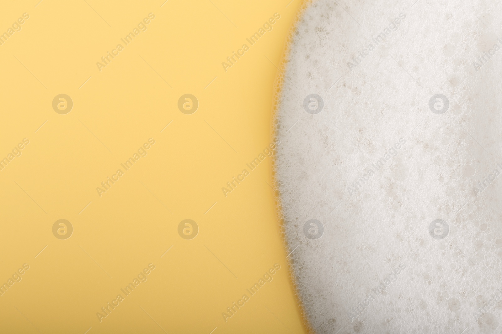 Photo of White fluffy foam on yellow background, top view. Space for text