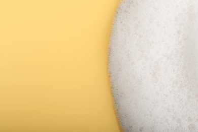 Photo of White fluffy foam on yellow background, top view. Space for text