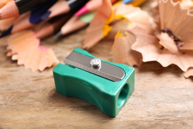 Photo of Turquoise sharpener, pencils and shavings on wooden table, closeup