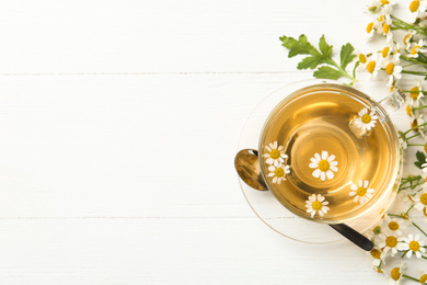 Photo of Flat lay composition with cup of tea and chamomile flowers on white wooden table. Space for text