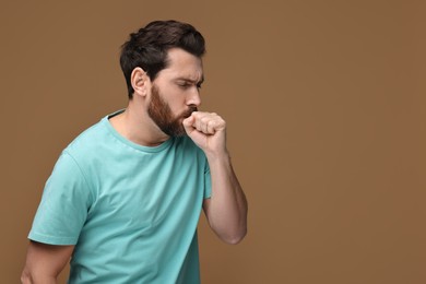 Sick man coughing on brown background, space for text. Cold symptoms