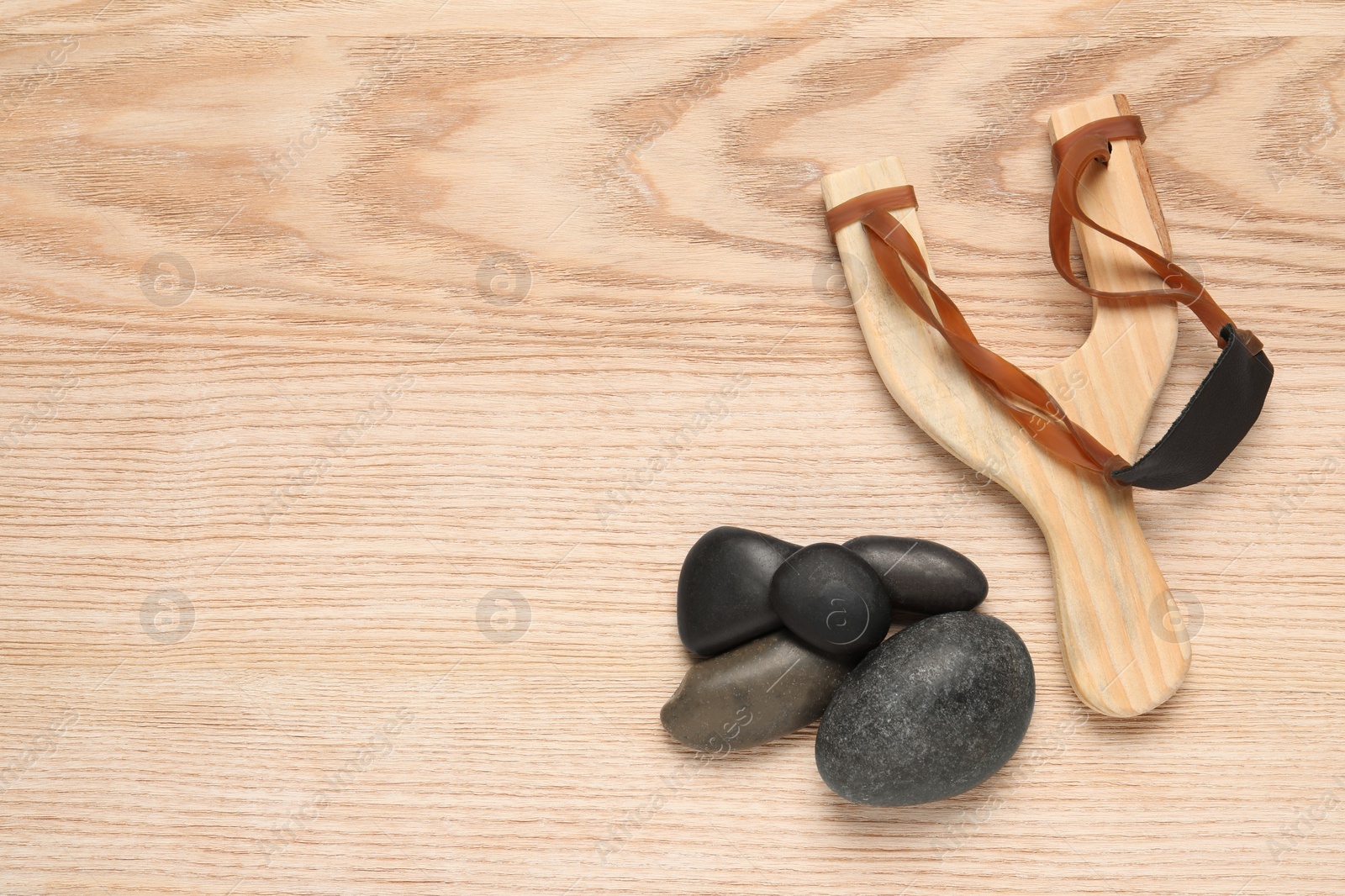 Photo of Slingshot with stones on wooden background, flat lay. Space for text