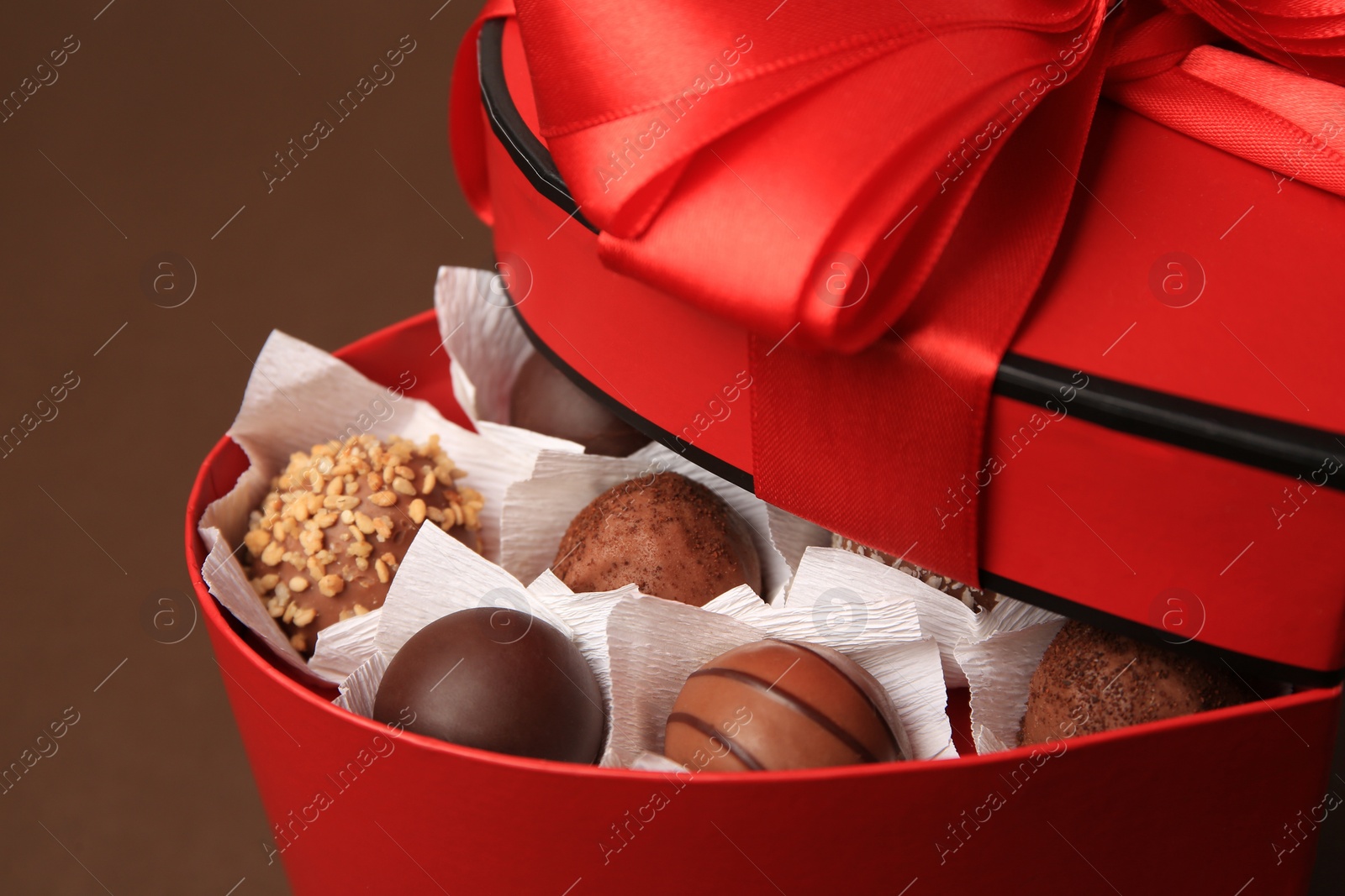 Photo of Heart shaped box with delicious chocolate candies on brown background, closeup