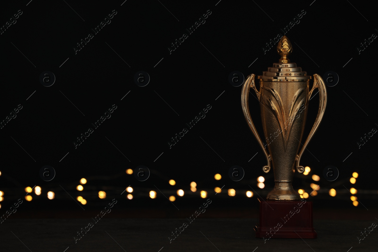 Photo of Golden trophy cup on table against blurred festive lights, space for text