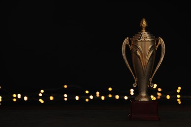 Photo of Golden trophy cup on table against blurred festive lights, space for text