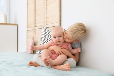 Photo of Cute boy kissing his little sister on bed at home