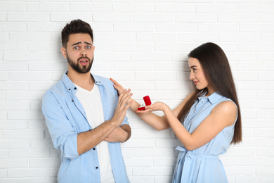 Photo of Young man rejecting engagement ring from girlfriend near white brick wall