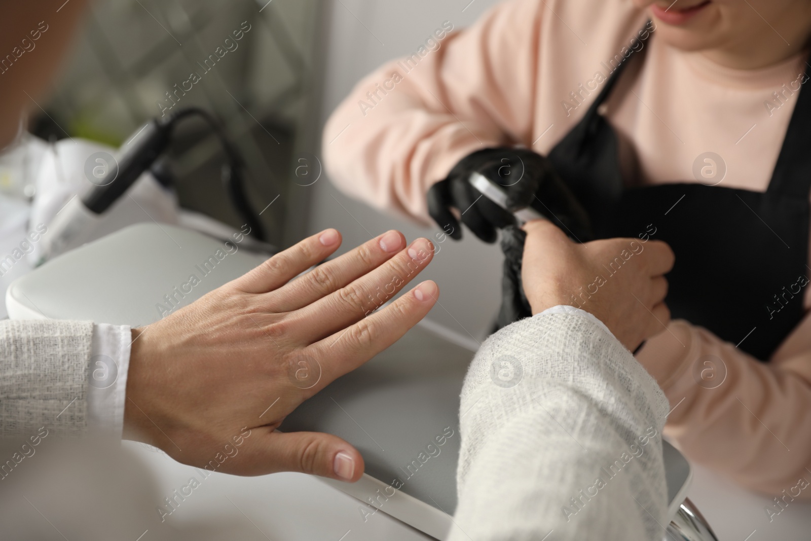 Photo of Professional manicurist filing client's nails in beauty salon, closeup