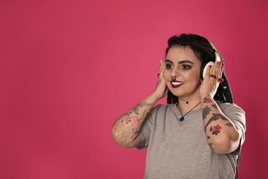 Photo of Beautiful young woman with tattoos on arms, nose piercing and dreadlocks listening to music against pink background. Space for text