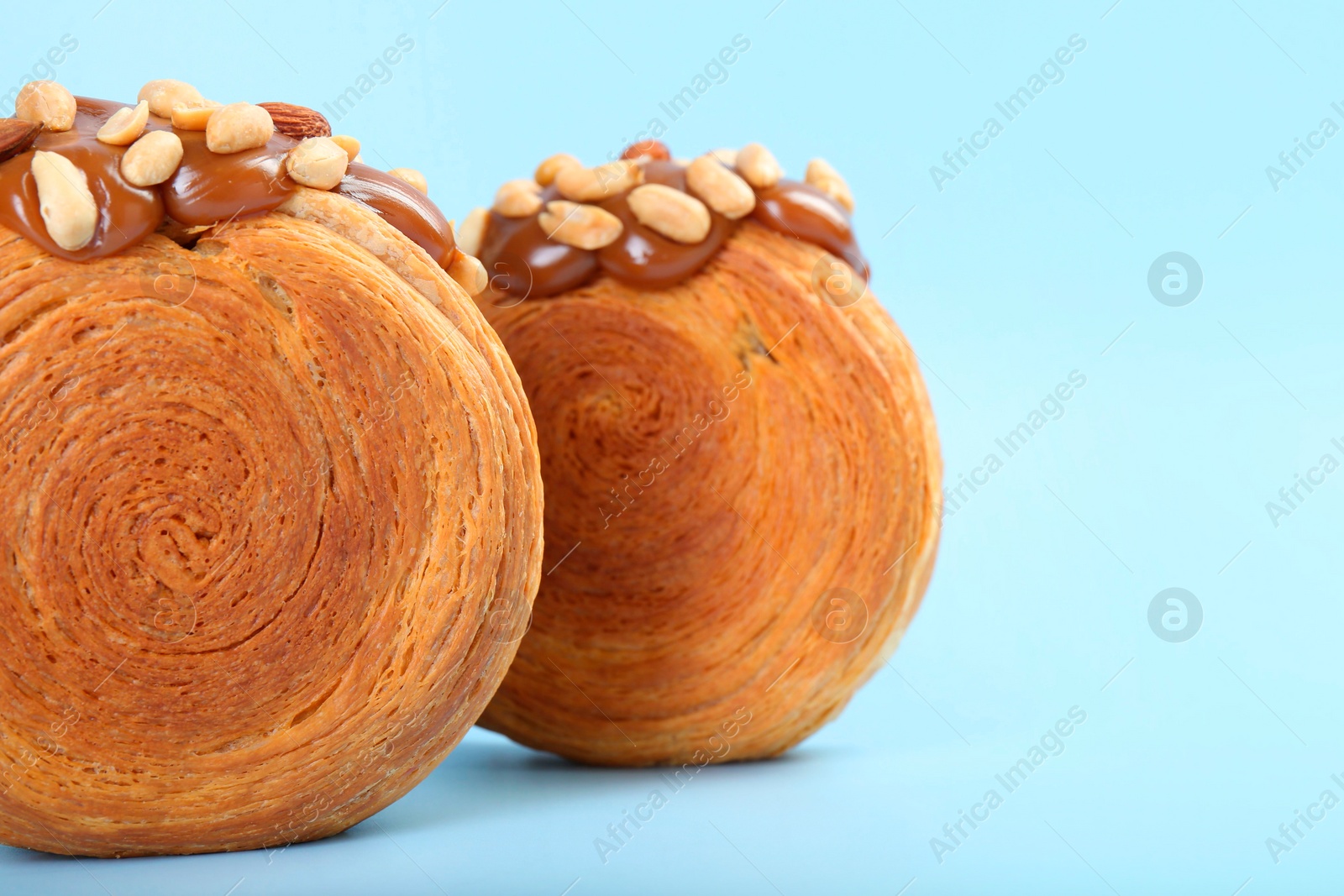 Photo of Tasty puff pastry. Supreme croissants with chocolate paste and nuts on light blue background, closeup. Space for text