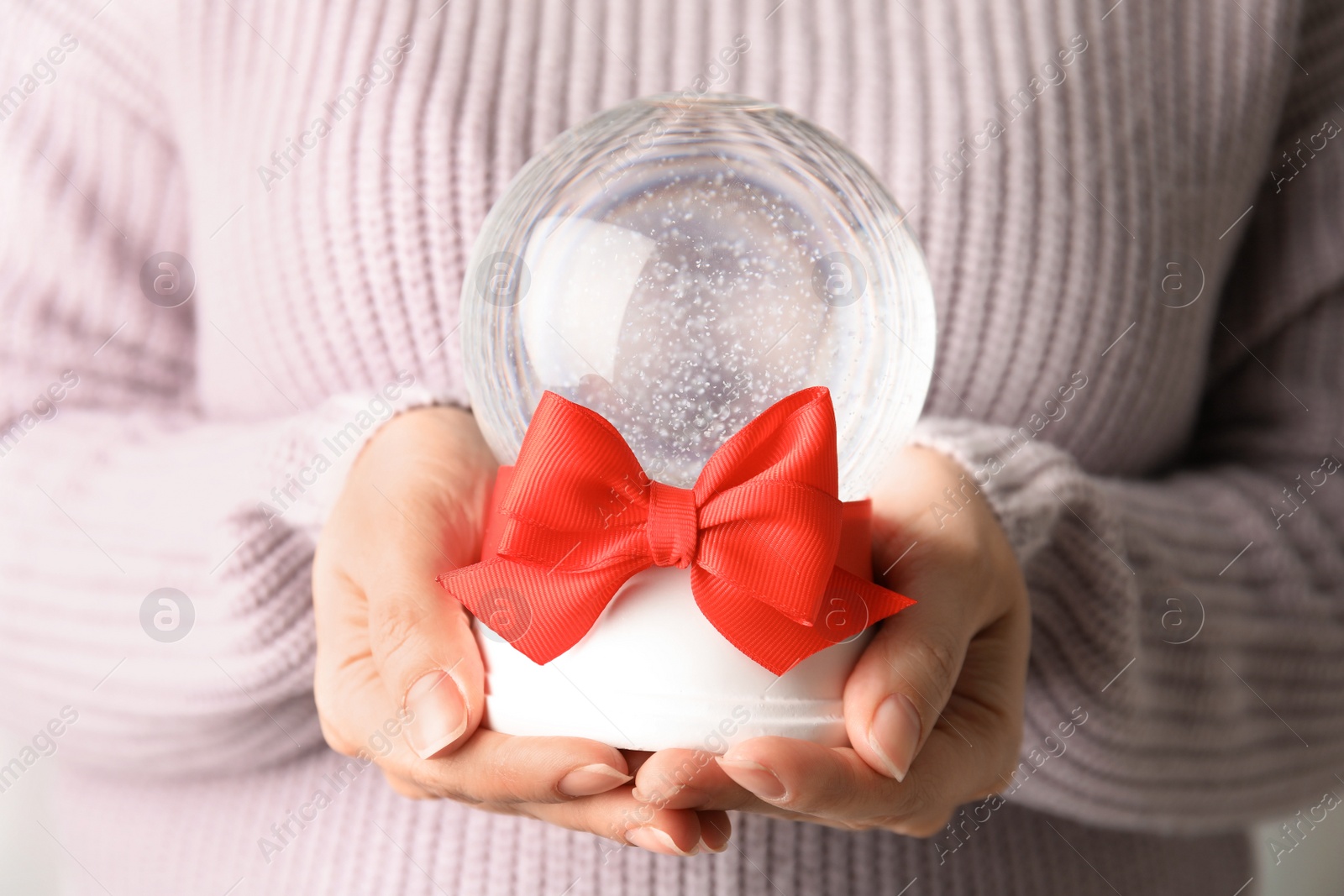 Photo of Woman holding empty snow globe with red bow, closeup