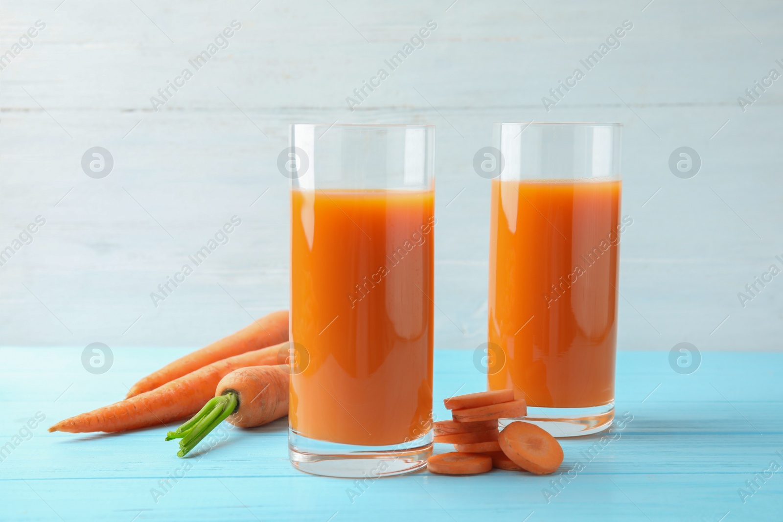 Photo of Glasses with carrot juice and fresh vegetable on wooden table