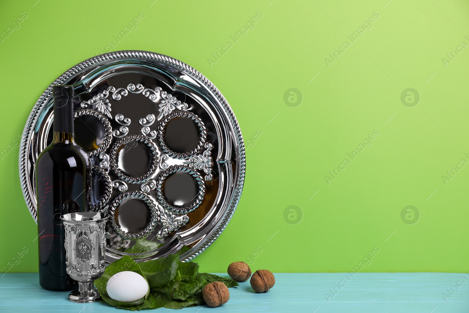 Photo of Symbolic Pesach (Passover Seder) items on light blue wooden table against green background, space for text