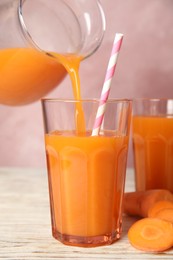 Photo of Pouring freshly made carrot juice into glass on wooden table