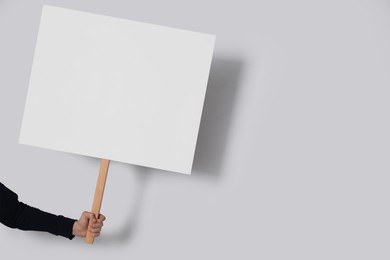 Woman holding blank sign on light grey background, closeup. Space for text