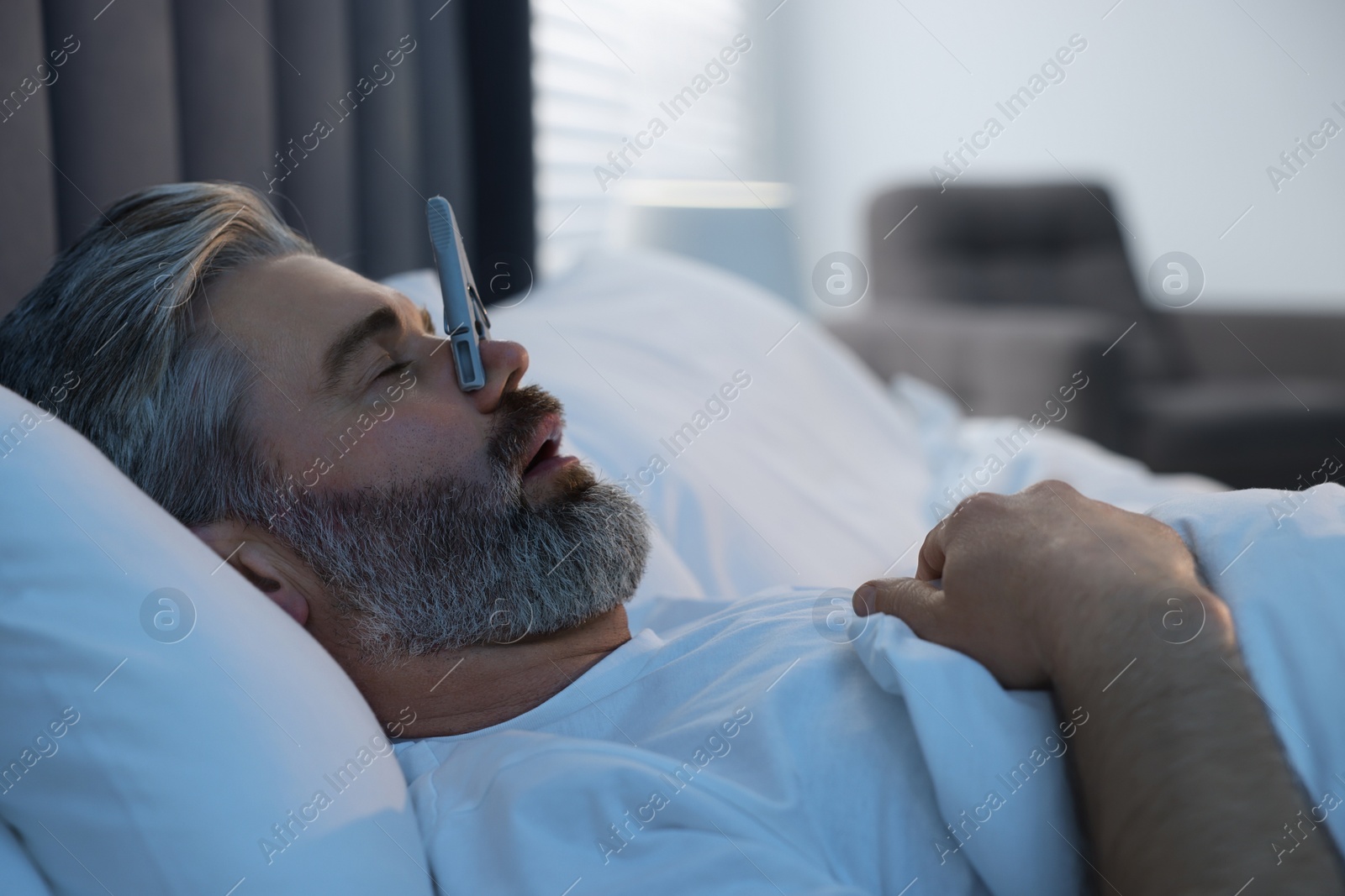 Photo of Man sleeping with clothespin on his nose in bed at home. Problem with snoring