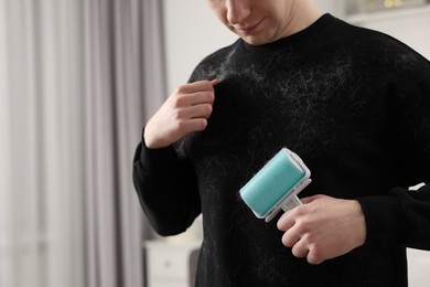 Photo of Pet shedding. Man with lint roller removing dog's hair from sweater at home, closeup