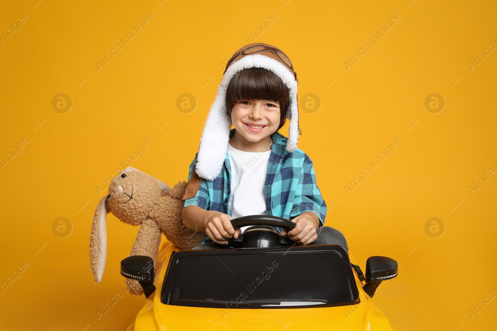 Photo of Cute little boy with toy bunny driving children's car on yellow background