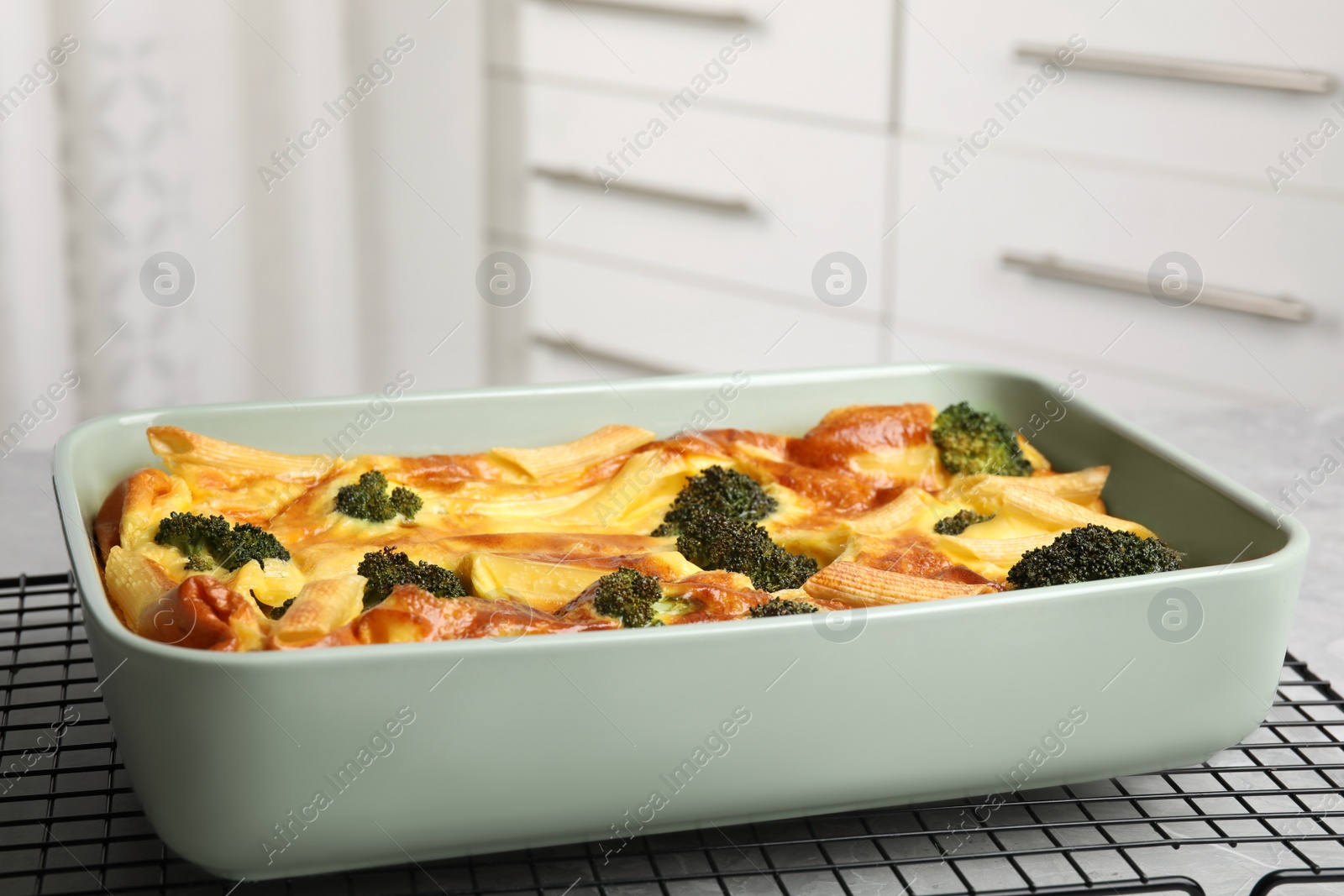 Photo of Tasty broccoli casserole in baking dish on cooling rack