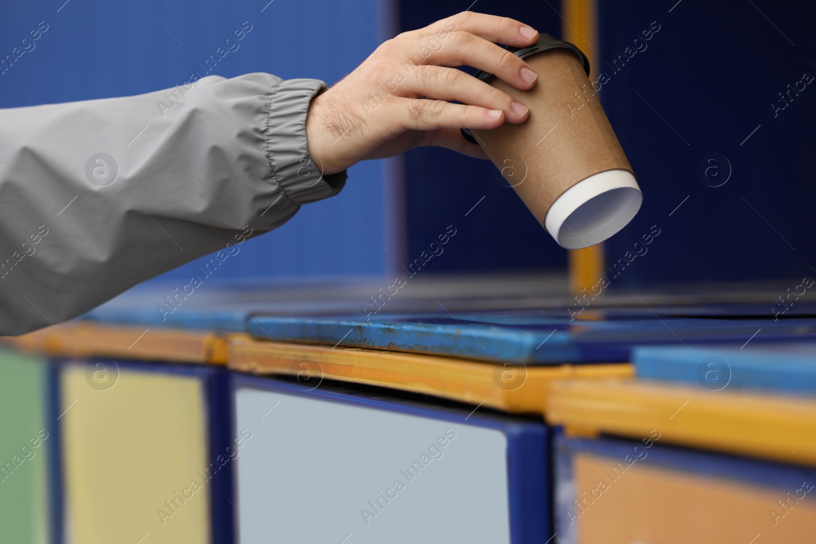 Photo of Man throwing paper coffee cup into garbage bin outdoors, closeup. Waste sorting