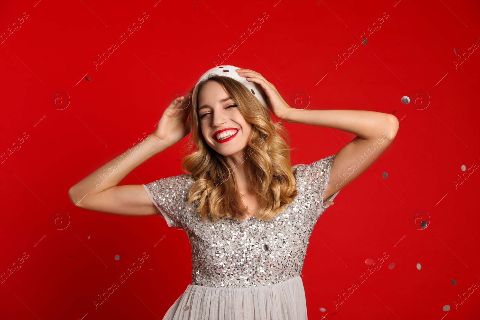 Photo of Happy young woman wearing Santa hat and confetti on red background. Christmas celebration