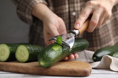 Woman peeling fresh cucumber at white wooden table, closeup