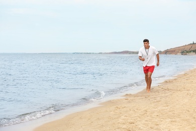 Photo of Handsome male lifeguard running on sandy beach