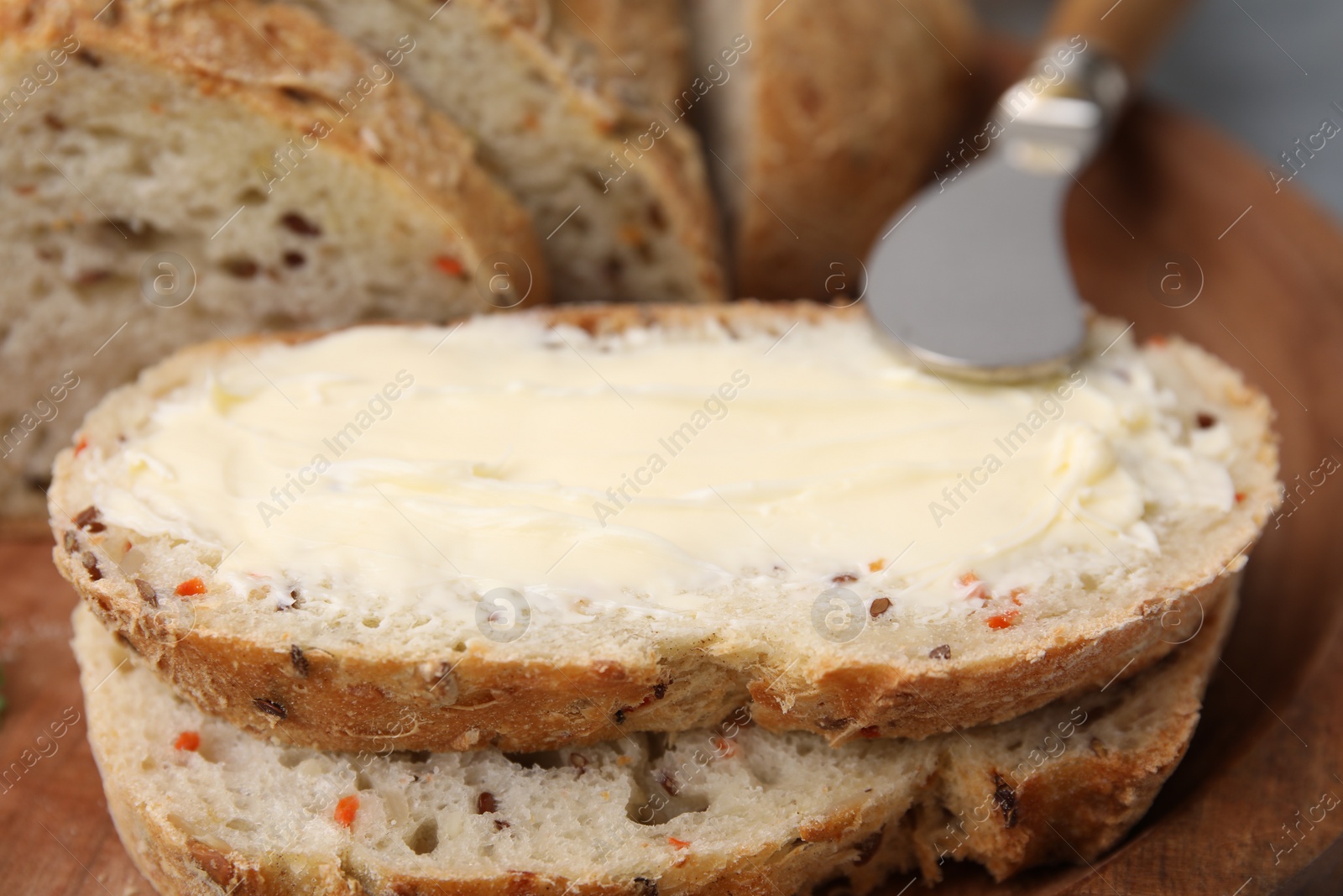 Photo of Tasty bread with butter and knife on wooden board, closeup