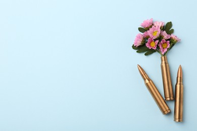 Bullets and cartridge case with beautiful flowers on light blue background, flat lay. Space for text