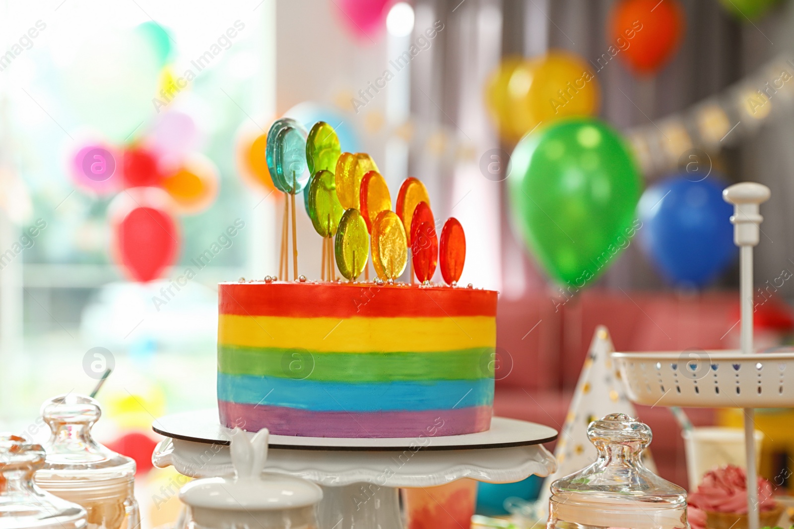 Photo of Bright birthday cake and other treats on table in decorated room