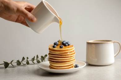 Woman pouring honey onto tasty pancakes with berries on table, closeup