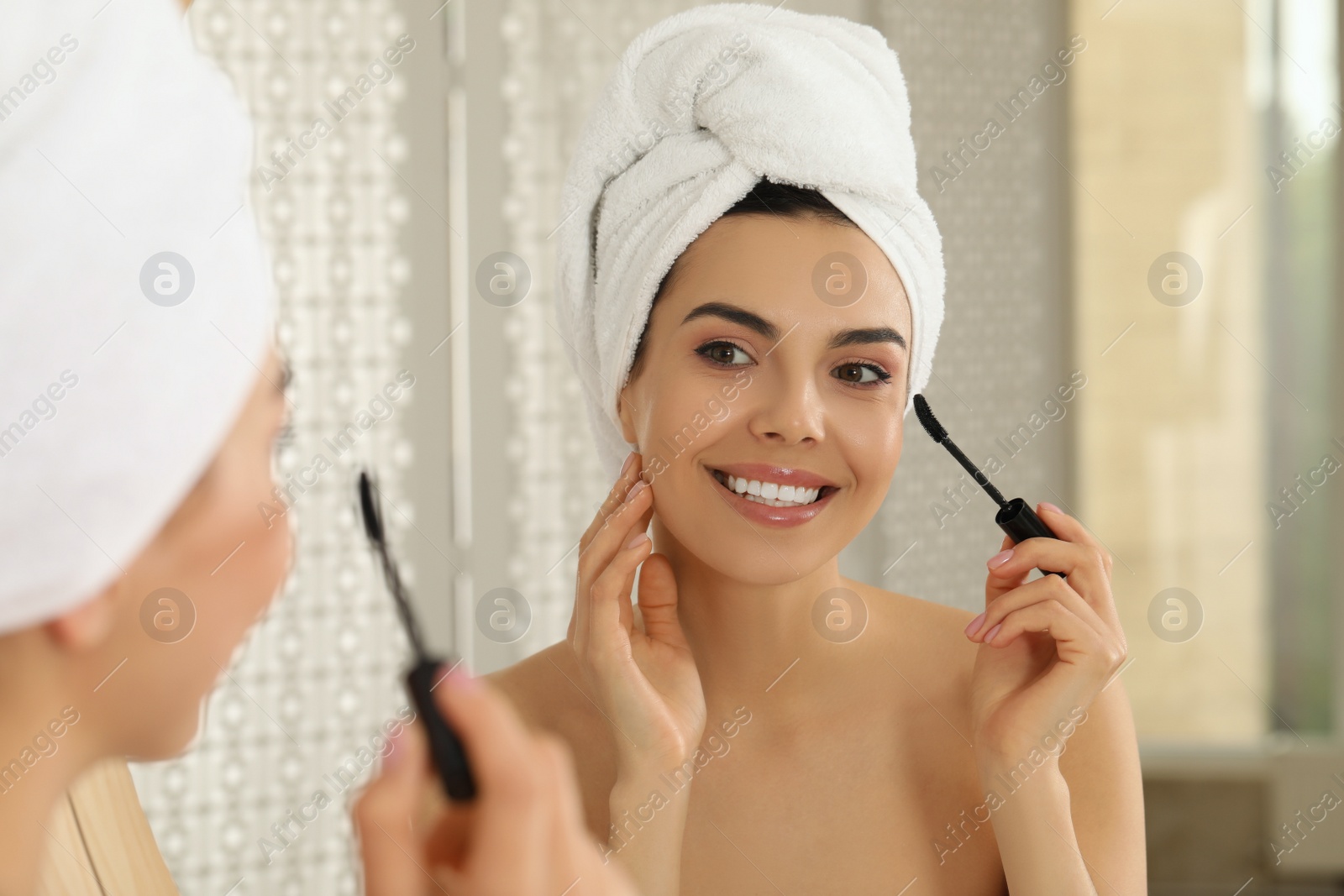 Photo of Beautiful young woman applying mascara in front of mirror at home