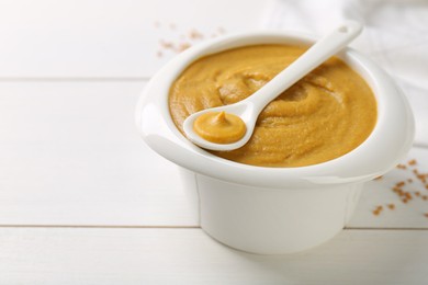 Photo of Spoon and bowl of tasty mustard sauce on white wooden table, space for text