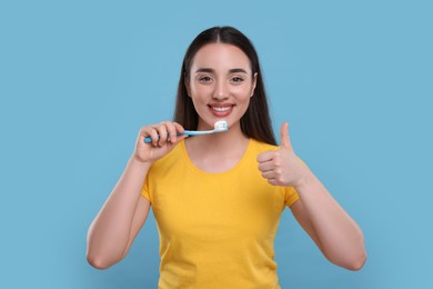 Photo of Happy young woman holding plastic toothbrush on light blue background