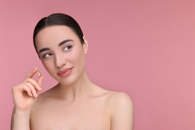 Photo of Beautiful young woman with vitamin pill on pink background. Space for text