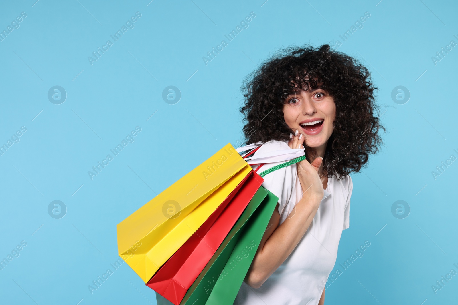 Photo of Happy young woman with shopping bags on light blue background. Space for text