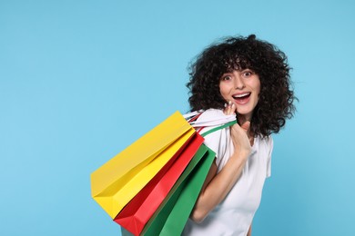 Happy young woman with shopping bags on light blue background. Space for text