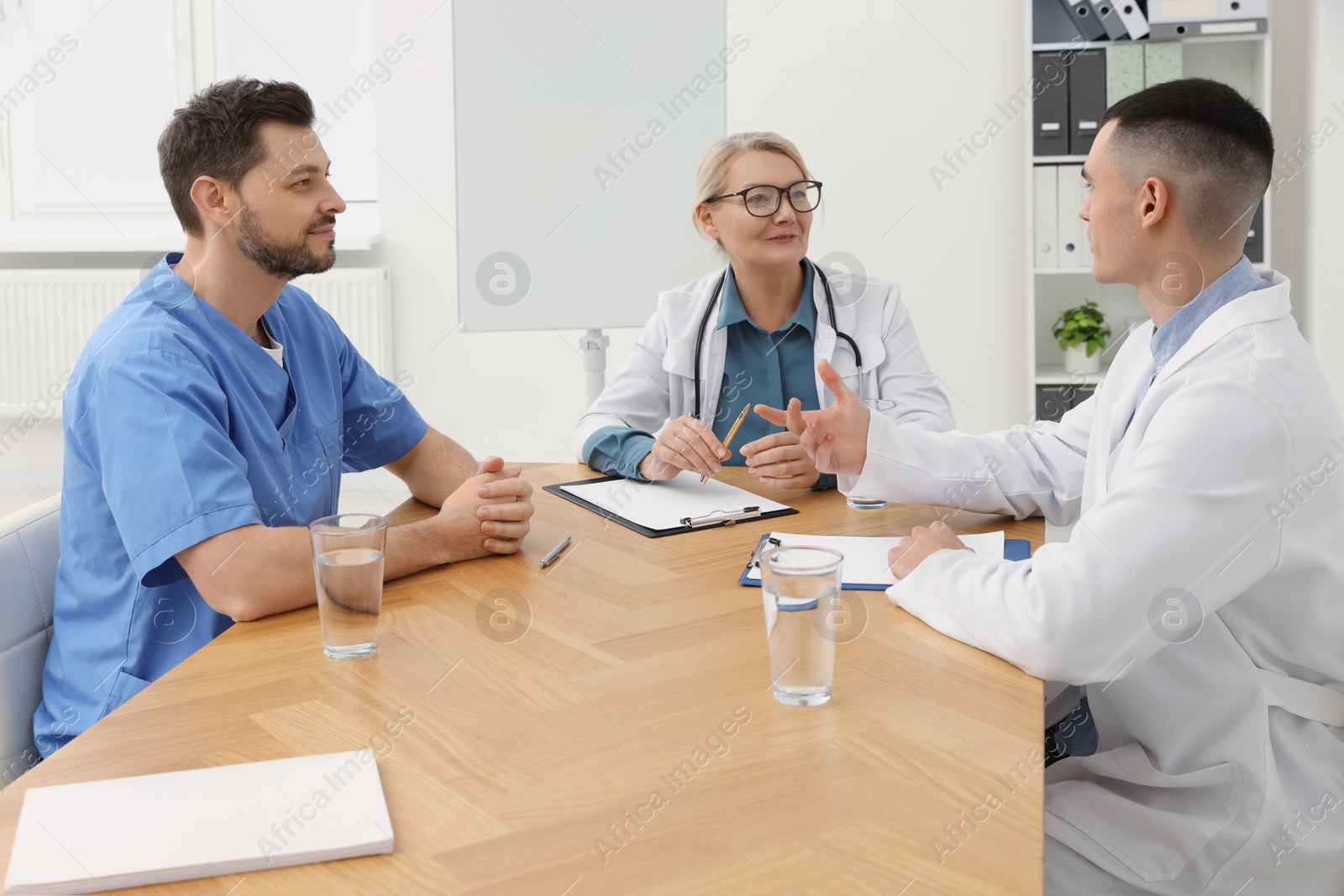 Photo of Medical conference. Team of doctors having discussion at wooden table in clinic