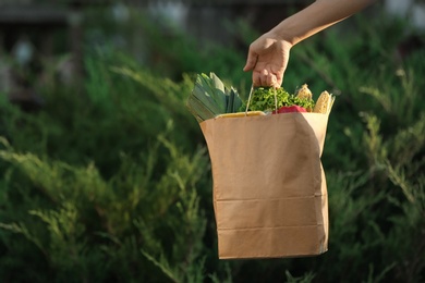 Photo of Woman holding paper bag with fresh vegetables outdoors, space for text
