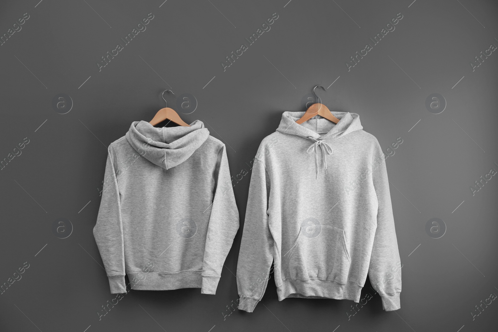 Photo of New hoodie sweaters with hangers on grey wall. Mockup for design