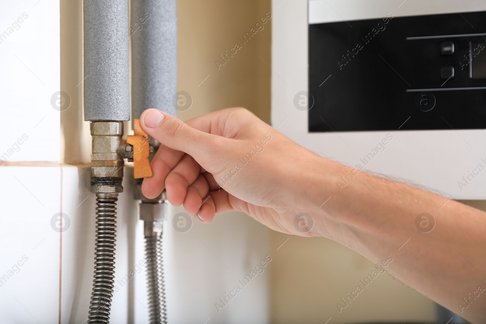 Photo of Man turning on valve of gas boiler indoors, closeup