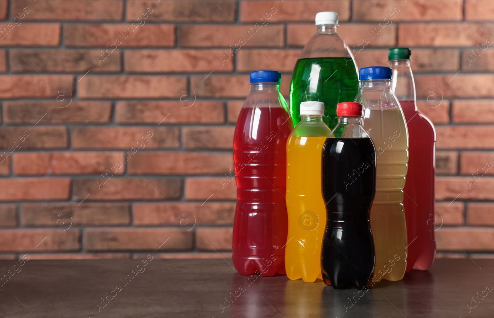 Photo of Bottles of soft drinks on table near brick wall. Space for text