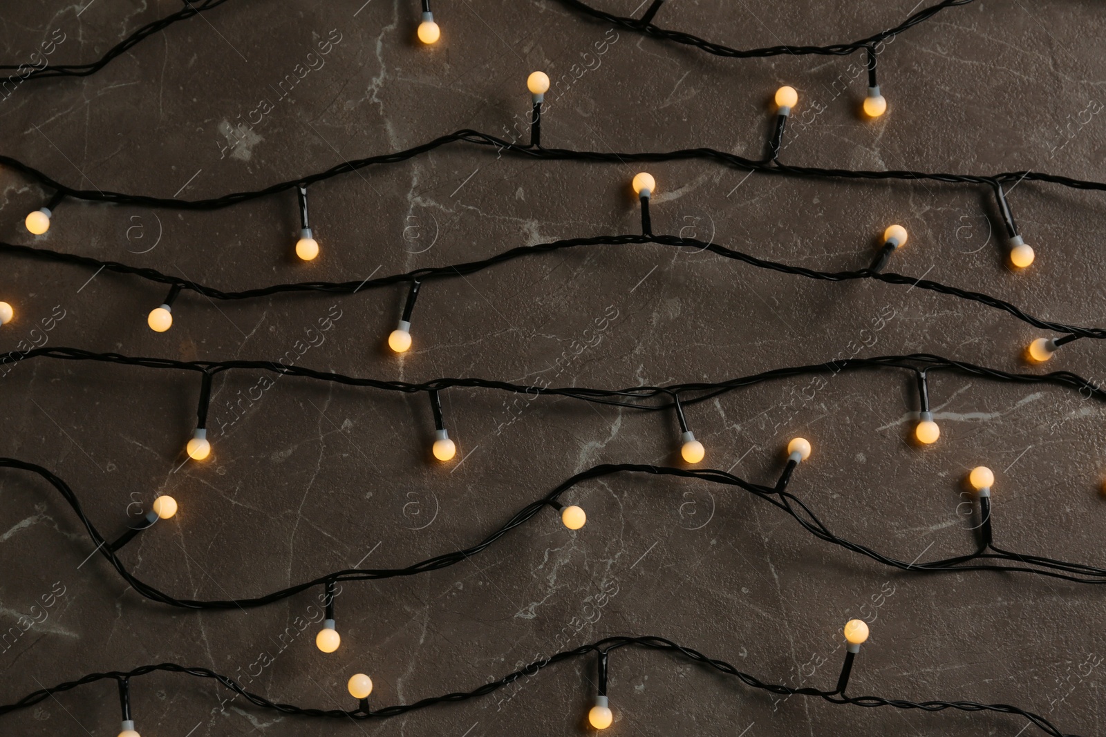 Photo of Glowing Christmas lights on grey marble background, top view