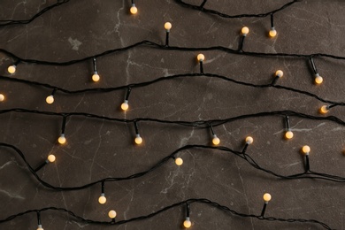 Glowing Christmas lights on grey marble background, top view