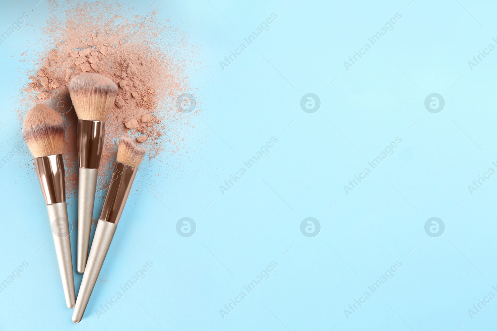 Photo of Brushes and scattered face powder on light blue background, flat lay. Space for text