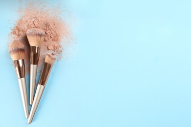 Photo of Brushes and scattered face powder on light blue background, flat lay. Space for text