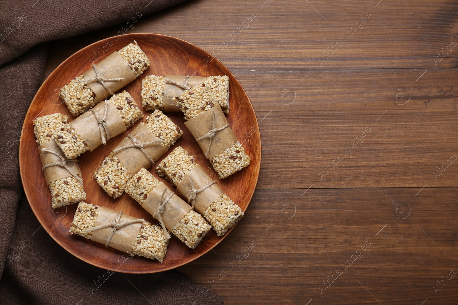 Photo of Plate with tasty sesame seed bars on wooden table, top view. Space for text