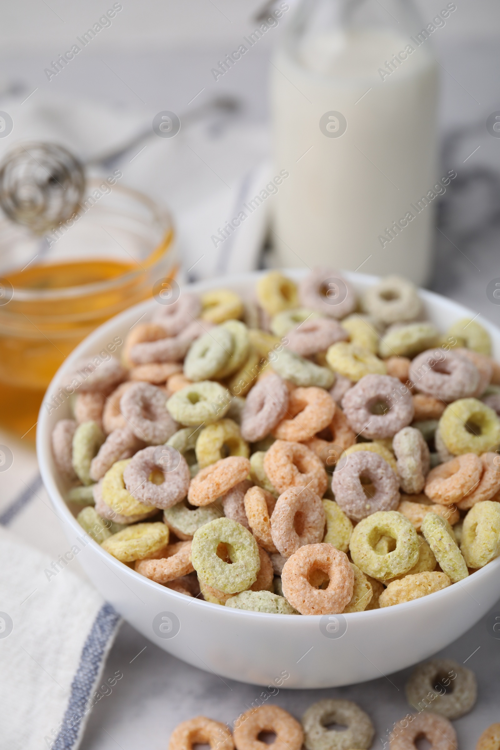 Photo of Tasty cereal rings in bowl, milk and honey on light table, closeup